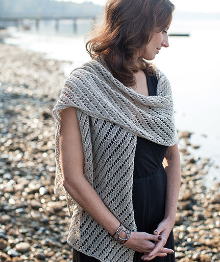 A person standing by a body of water wearing a beige, lace-patterned scarf draped over the shoulders.